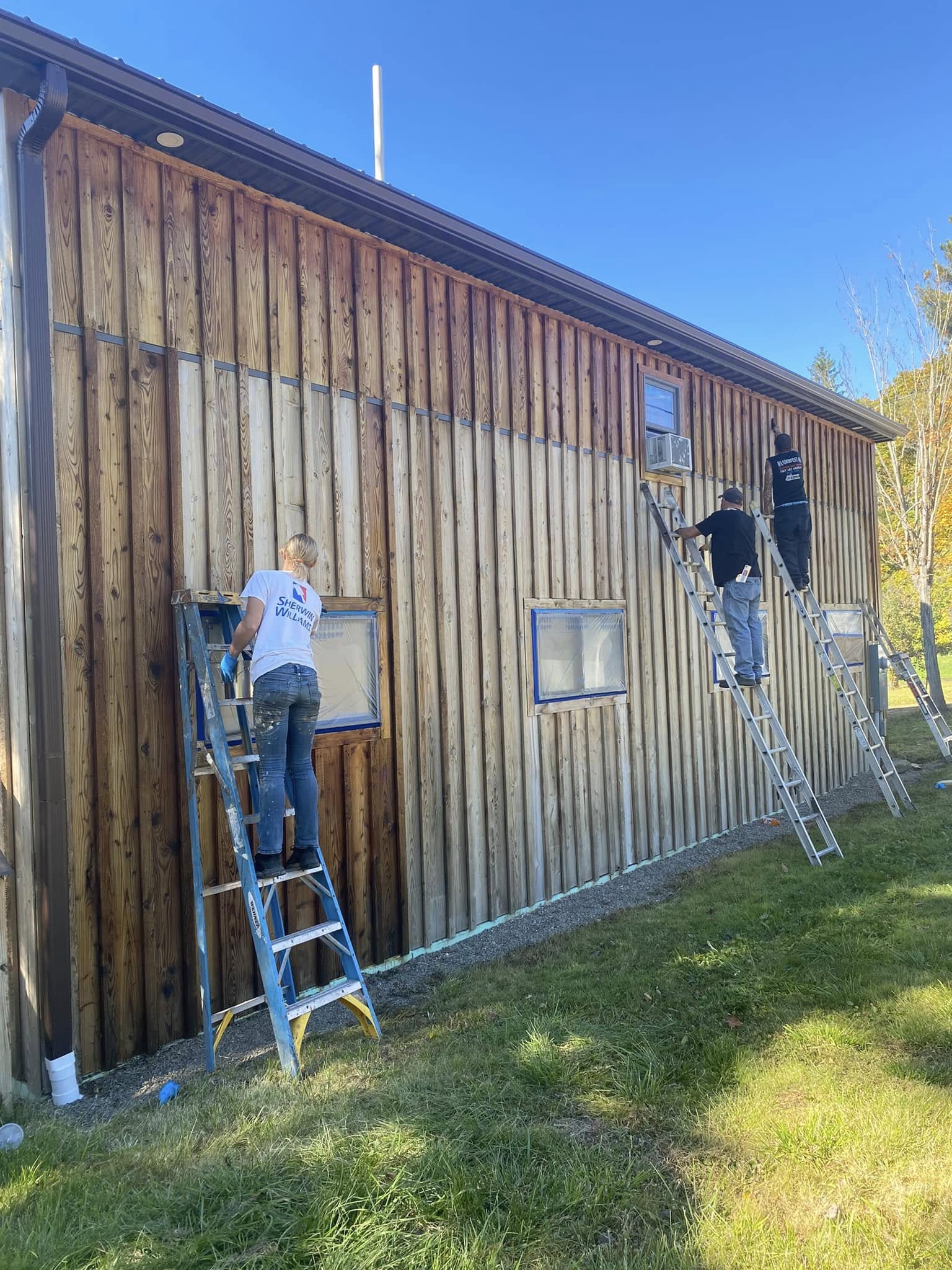 Crew staining dark finish onto vertical wood siding on a large building