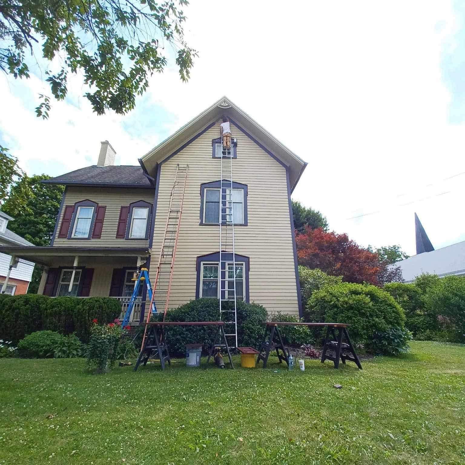 Painter working on a large two-story home exterior in Allegany County